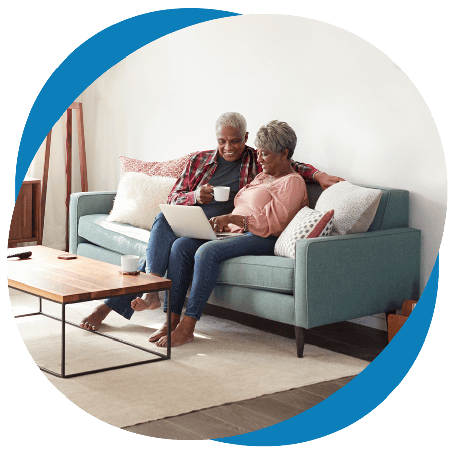 An older couple sharing a sofa, engaged in internet browsing on a laptop while savoring their coffee